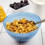 honey almond granola in a blue bowl with a spoon and berries in the background