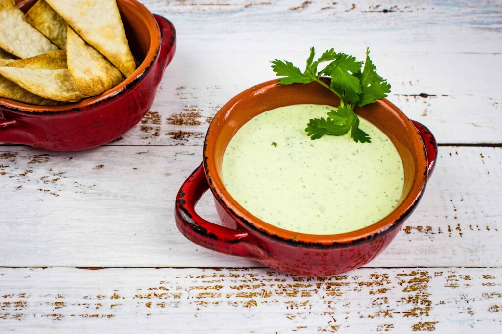 jalapeno dip in a rustic red bowl with chips in the background