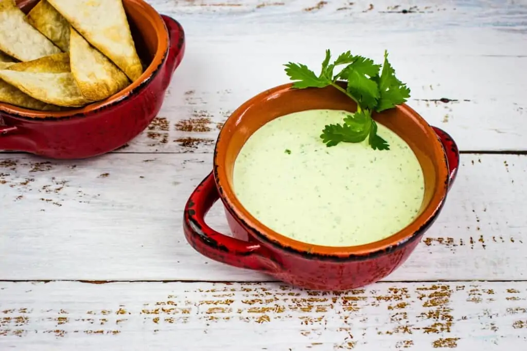 jalapeno dip in a rustic red bowl with chips in the background