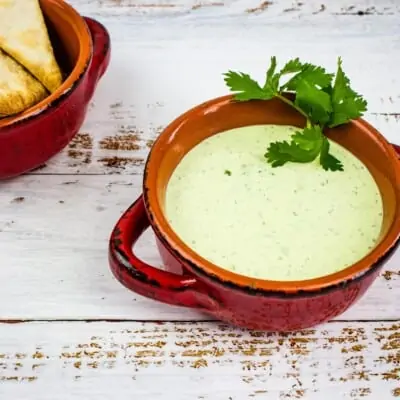 jalapeno dip in a rustic red bowl with chips in the background