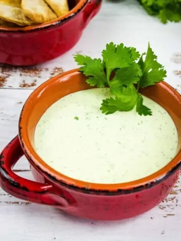 a closeup shot of creamy jalapeno dip in a rustic bowl with tortilla chips in the background