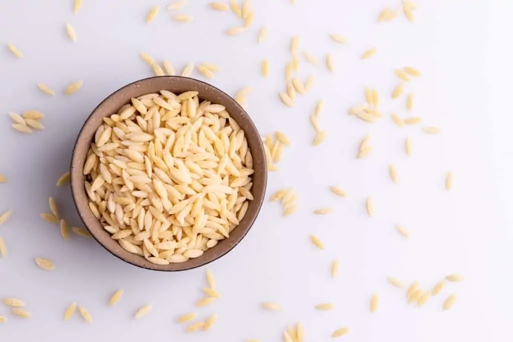 orzo pasta in a bowl and some scattered on the surface