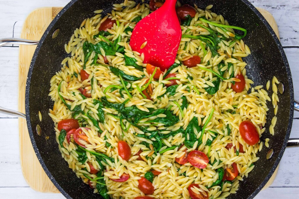 adding the tomatoes and mixing to combine and make creamy spinach orzo with tomatoes.