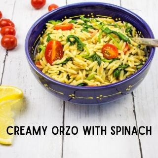 Creamy orzo with spinach and tomatoes in a serving bowl with a spoon
