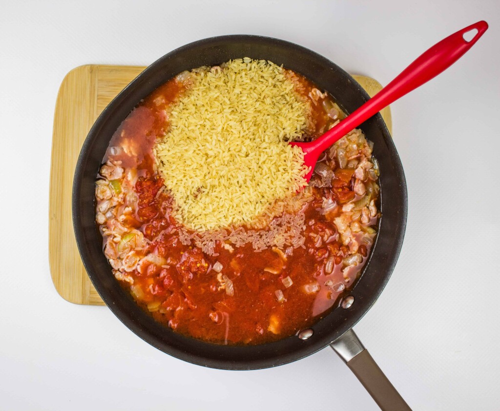 adding the rice, tomatoes, green bell pepper and liquid to the skillet