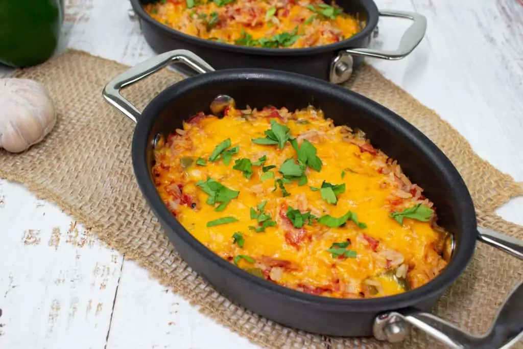 Cheesy Spanish rice in an oval casserole dish with a second one in the background.