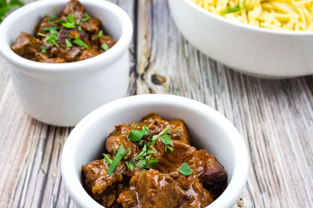 Authentic Hungarian Goulash in white serving bowls with spaetzel in the background