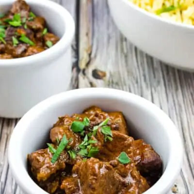 Authentic Hungarian Goulash in white serving bowls with spaetzel in the background