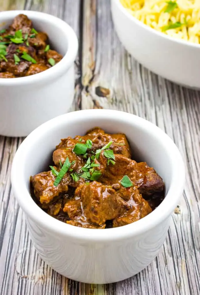 authentic hungarian goulash in white serving bowls with a bowl of spaetzle in the background