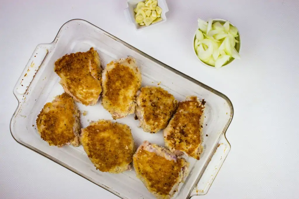 golden brown chicken in a single layer in a casserole dish with onion and garlic on the side