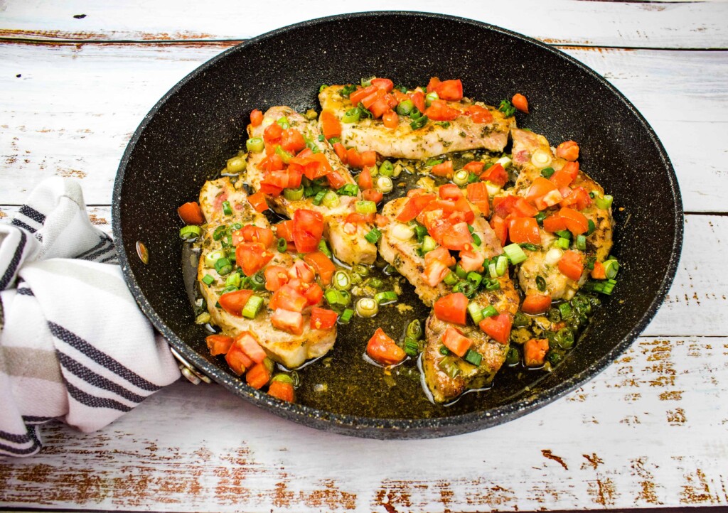 Pork Chops with Tomato & Green onion relish on a black skillet.