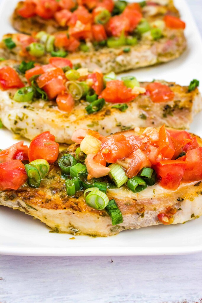 a closeup of pork chops with tomato & green onion relish