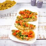 Pork chops with Tomato & Green Onion Relish on a white platter with couscous in the background