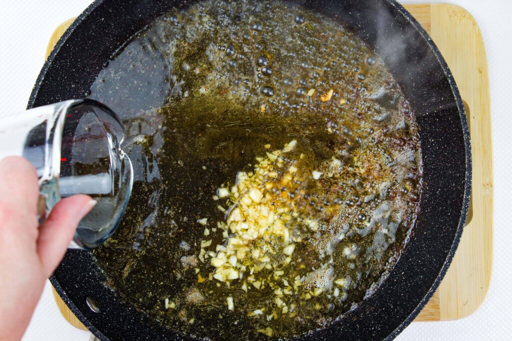 Sauteed garlic in a black skillet with white wine being poured in