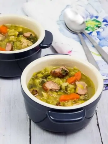 split pea, ham and sausage soup in two small bowls with spoons and a napkin in the background