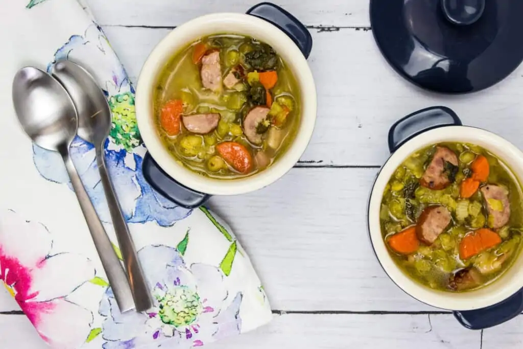 Split pea, ham and sausage soup in two small bowls with spoons and a napkin.