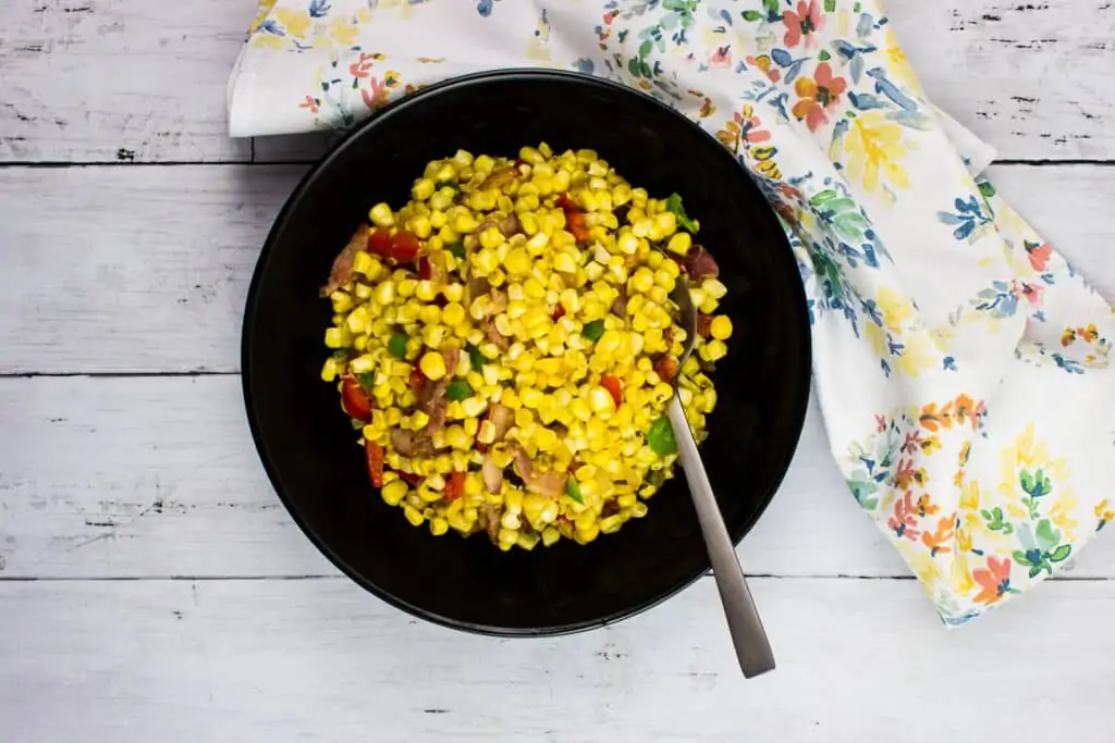 Corn salad in a black bowl with a fork.