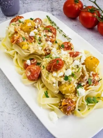 baked feta pasta on a rectangular platter with tomatoes in the background