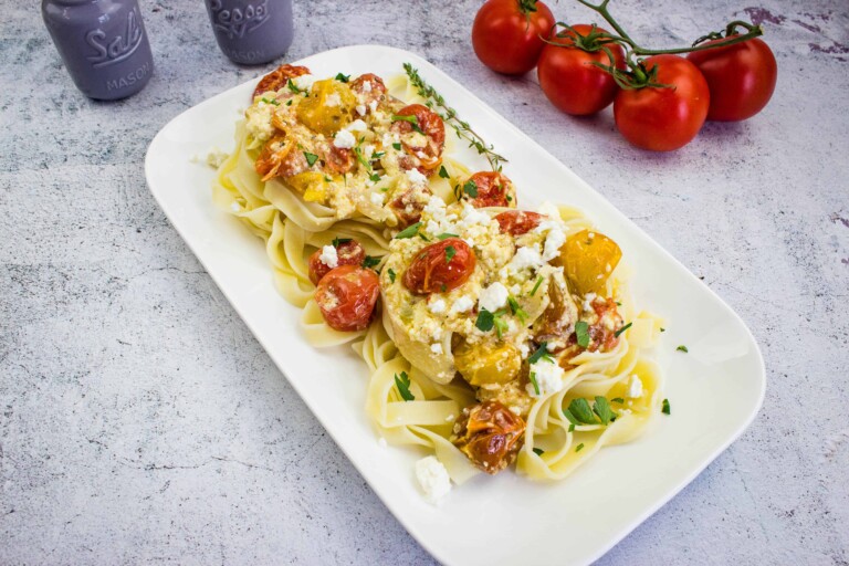 baked feta pasta on a rectangular platter with tomatoes in the background