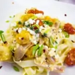 baked feta pasta on a square plate with tomatoes in teh background