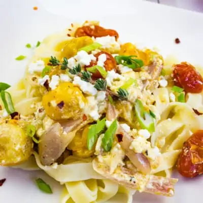 baked feta pasta on a square plate with tomatoes in teh background