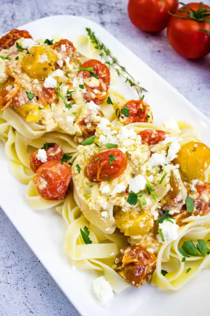 baked feta pasta on a square plate with tomatoes in the background