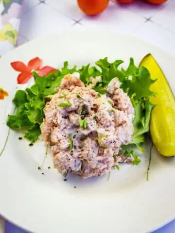 a scoop of old fashioned ham salad on a plate with a pickle and greens