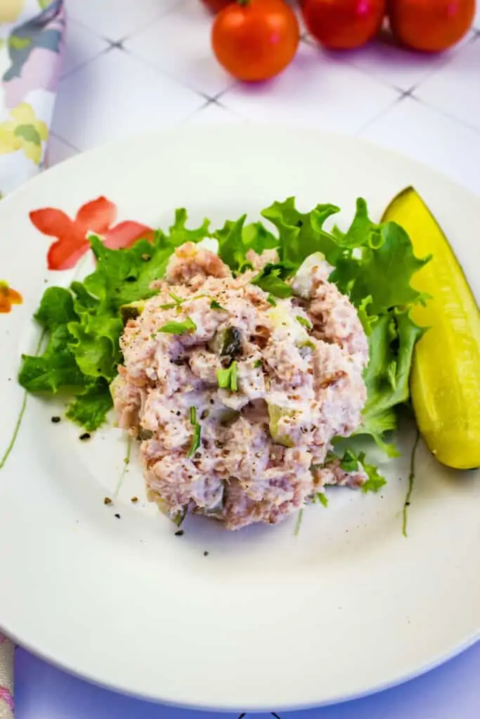 A closeup of old fashioned ham salad on a plate with a pickle.