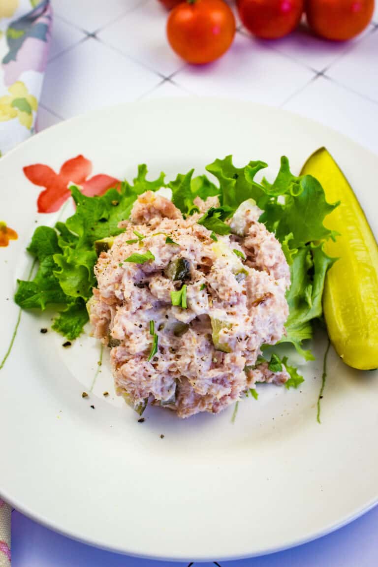 a scoop of old fashioned ham salad on a plate with a pickle and greens