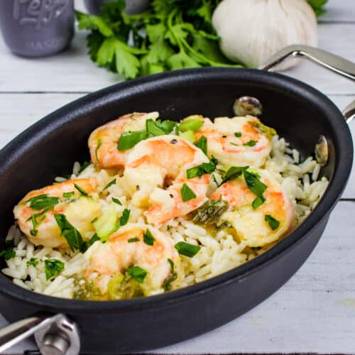 Fresh shrimp with rice, herbs, and vegetables in a black cooking skillet. Perfect for quick, flavorful meals.