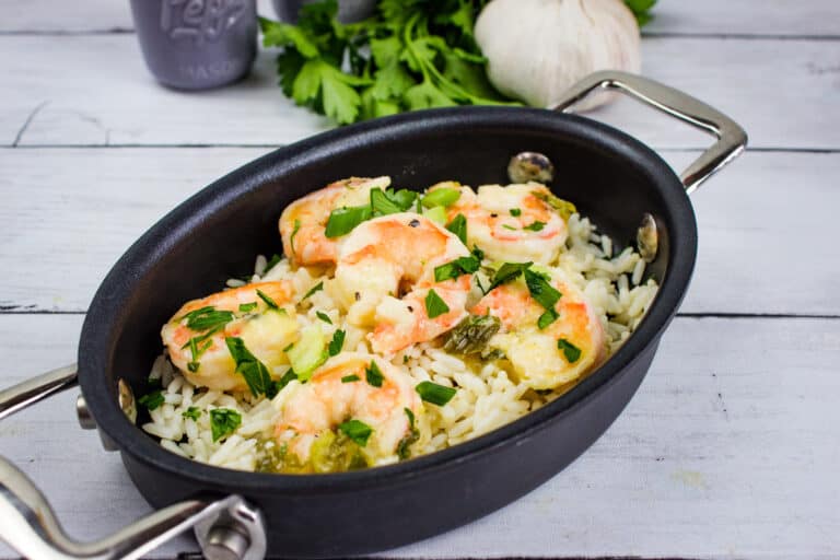 Fresh shrimp with rice, herbs, and vegetables in a black cooking skillet. Perfect for quick, flavorful meals.