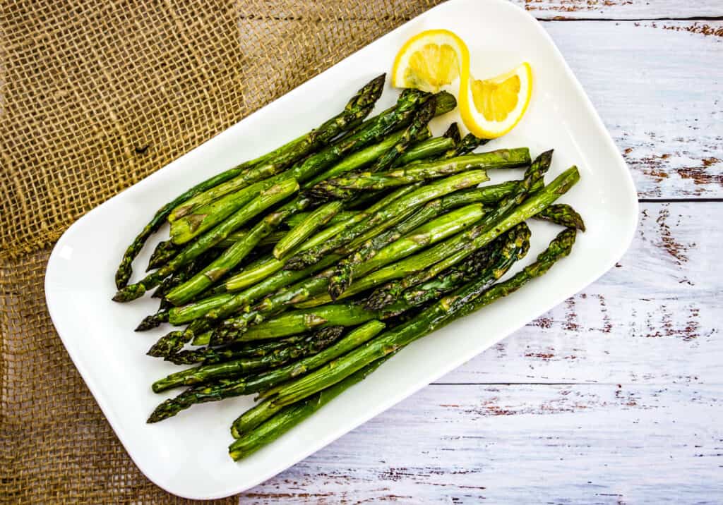 Smoked asparagus with lemon slice on a platter.