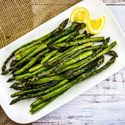 Smoked asparagus with lemon slice on a platter.
