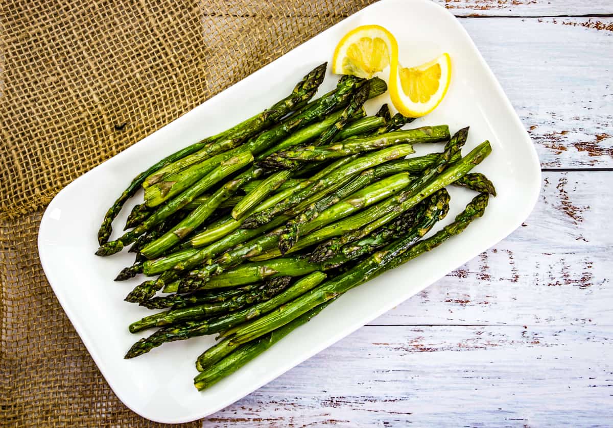 Smoked asparagus on a white platter with lemon.