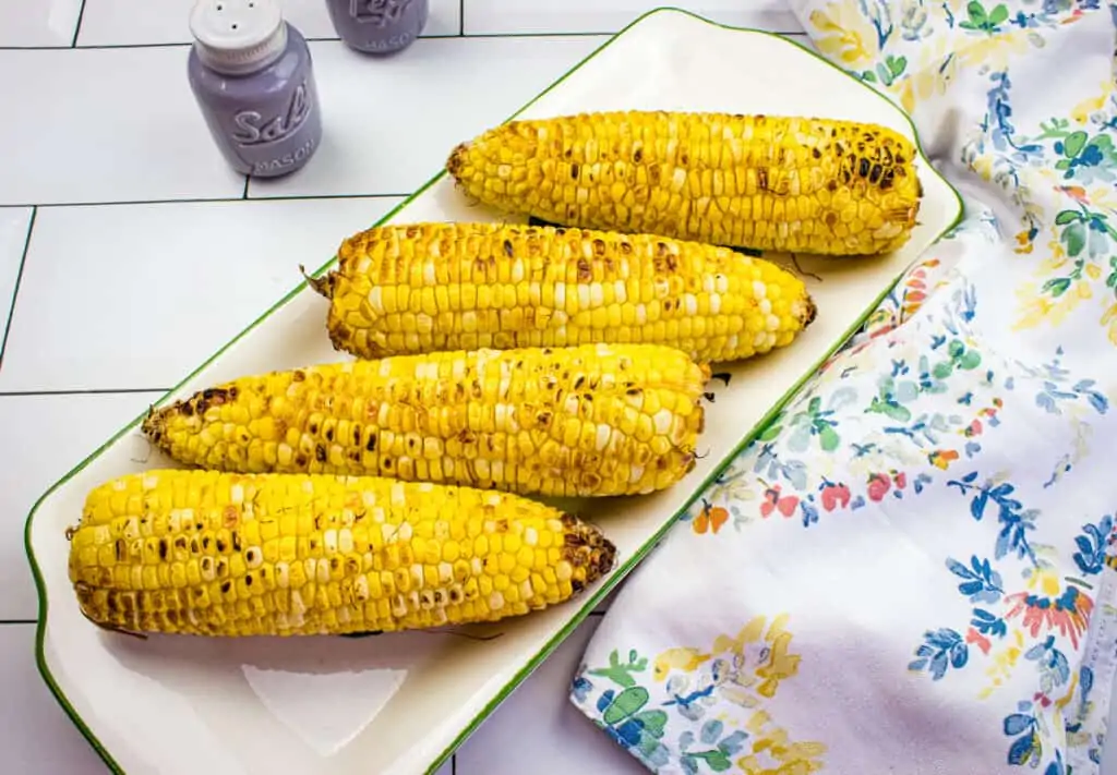 Roasted air fryer corn on the cob with char marks, served on a white dish with colorful napkin, perfect for outdoor eating.