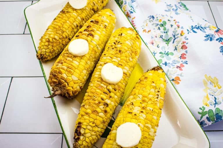 Grilled corn on a white platter.