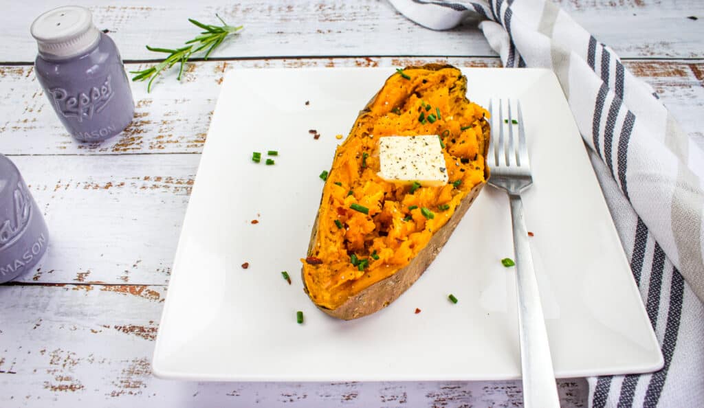 Healthy sweet potato with mashed sweet potatoes, herbs, and butter on a white plate. Perfect for nutritious meals.