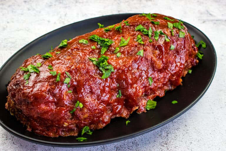 Smoked meatloaf with bacon garnished with herbs on a black plate.