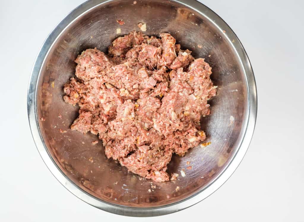 A stainless steel bowl filled with a mixture of raw ground meat and seasonings, ready to be shaped into a flavorful smoked meatloaf, viewed from above.