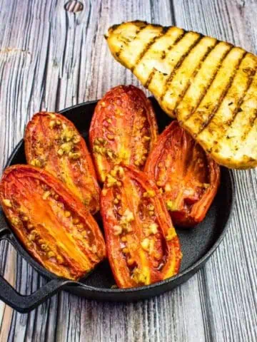 smoked tomatoes in a black bowl with grilled bread on the side