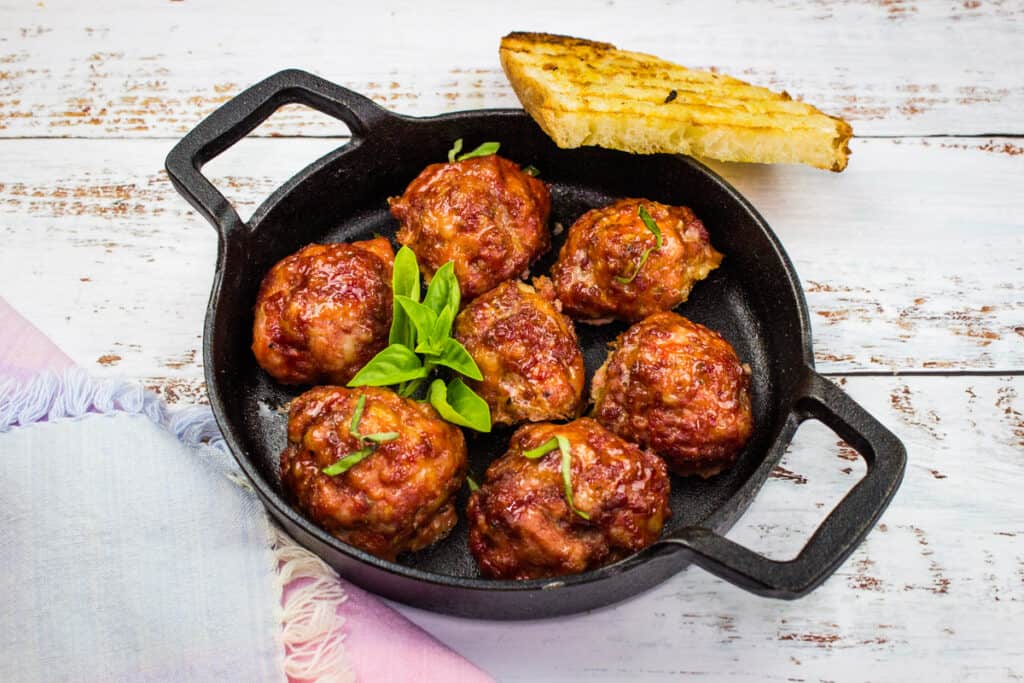 Smoked meatballs sizzling in a skillet on a wooden table.