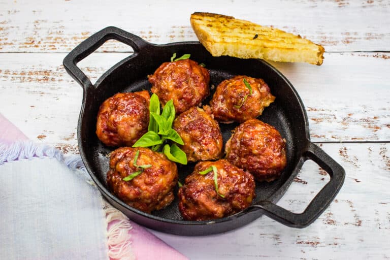 Smoked meatballs sizzling in a skillet on a wooden table.
