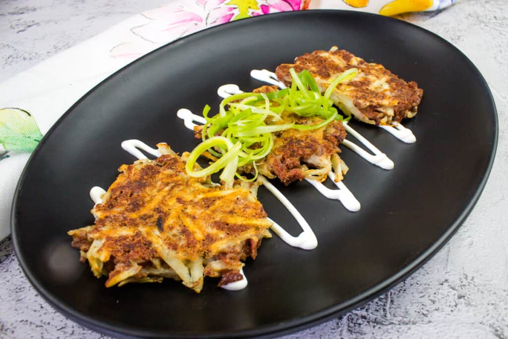 Three pieces of corned beef fritters, garnished with herbs on a black plate.