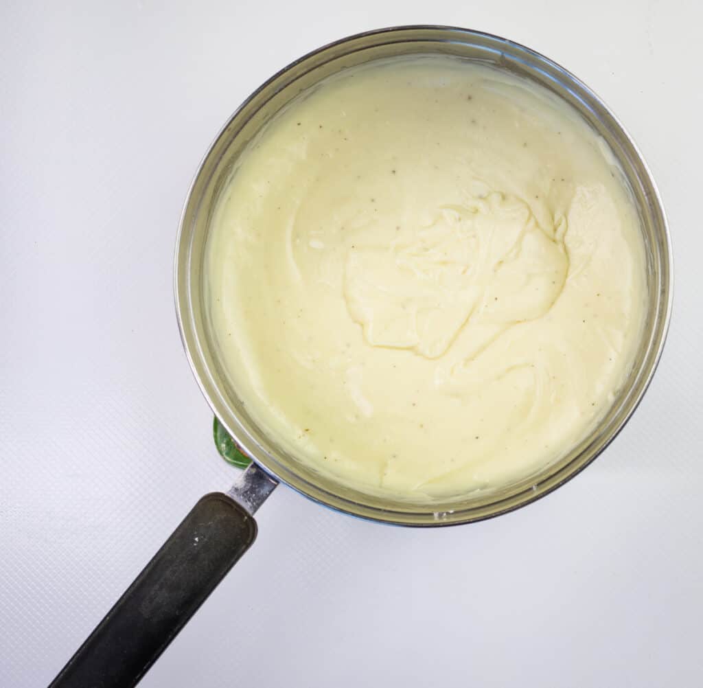 A saucepan filled with creamy white sauce, possibly creamed corn, viewed from above against a plain white background.