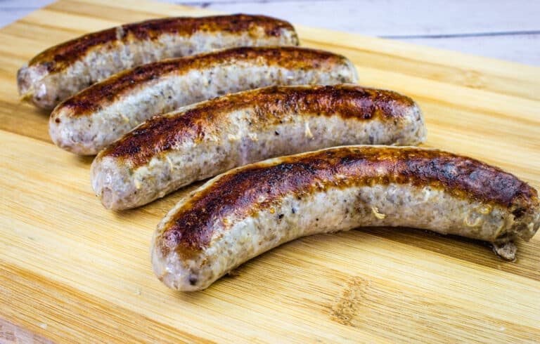 Four browned sous vide sausages are lined up on a wooden cutting board.