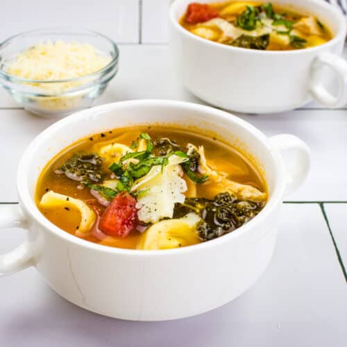 Tortellini soup with kale and chicken in white soup bowls.