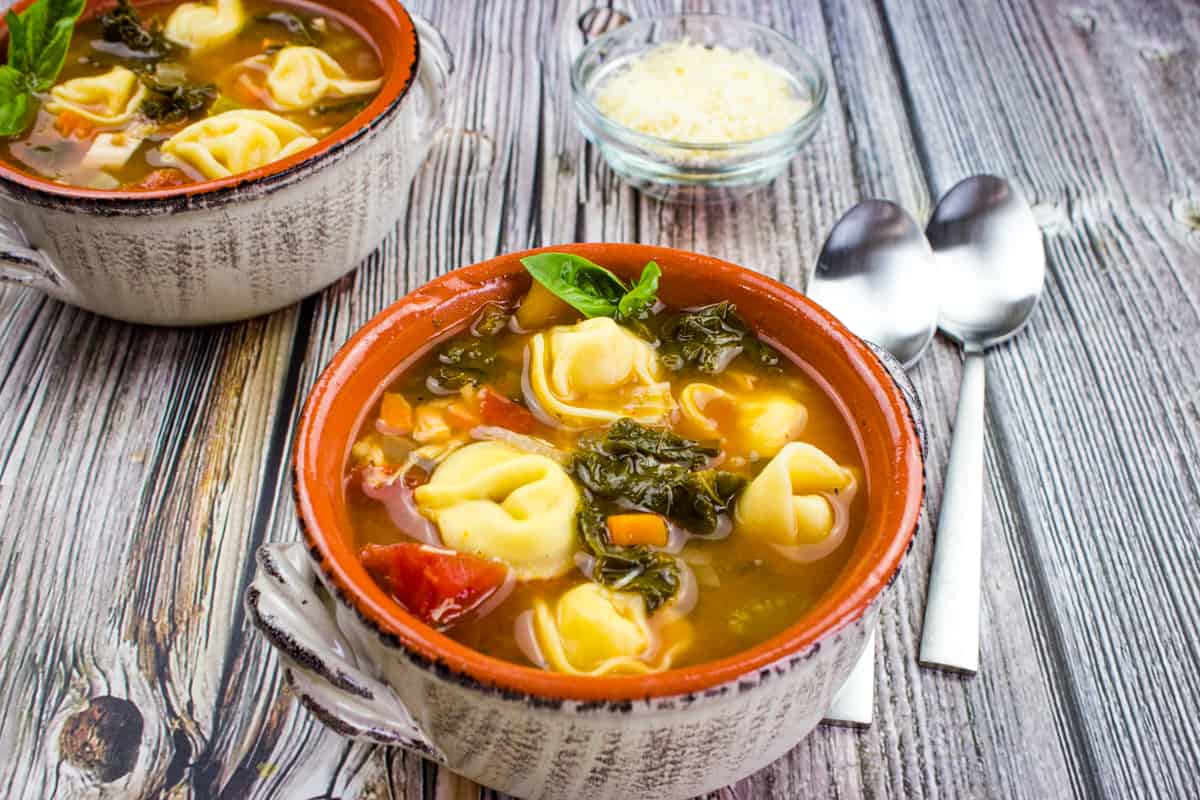 Kale and tortellini soup in a bowl on a wooden table.