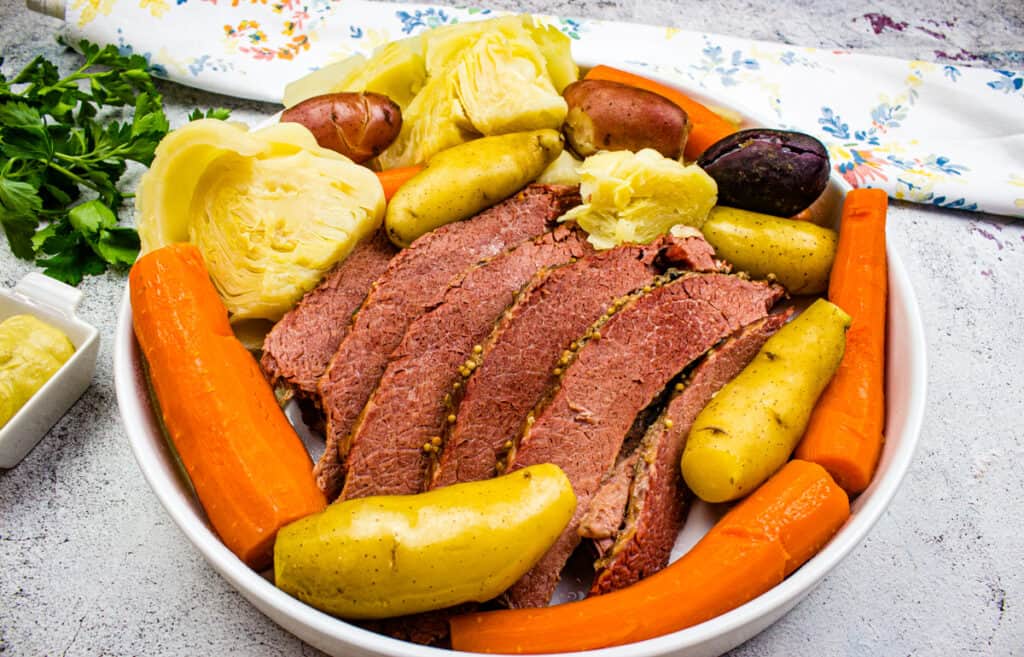 A bowl of corned beef and cabbage on a wooden cutting board with vegetables.