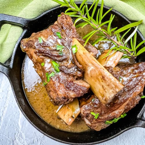 Garlic braised short ribs on a black platter, garnished with herbs.