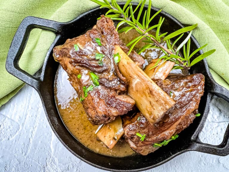 Garlic braised short ribs on a black platter, garnished with herbs.